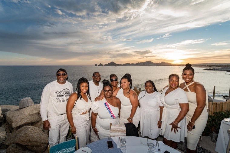 A group dressed in white gathered by the sea at sunset.