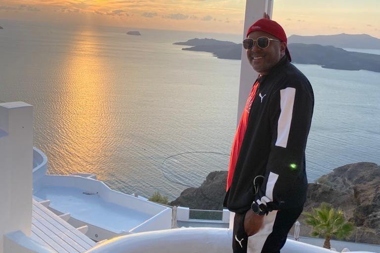 A traveler on a Santorini terrace at sunset, the caldera and sea behind.